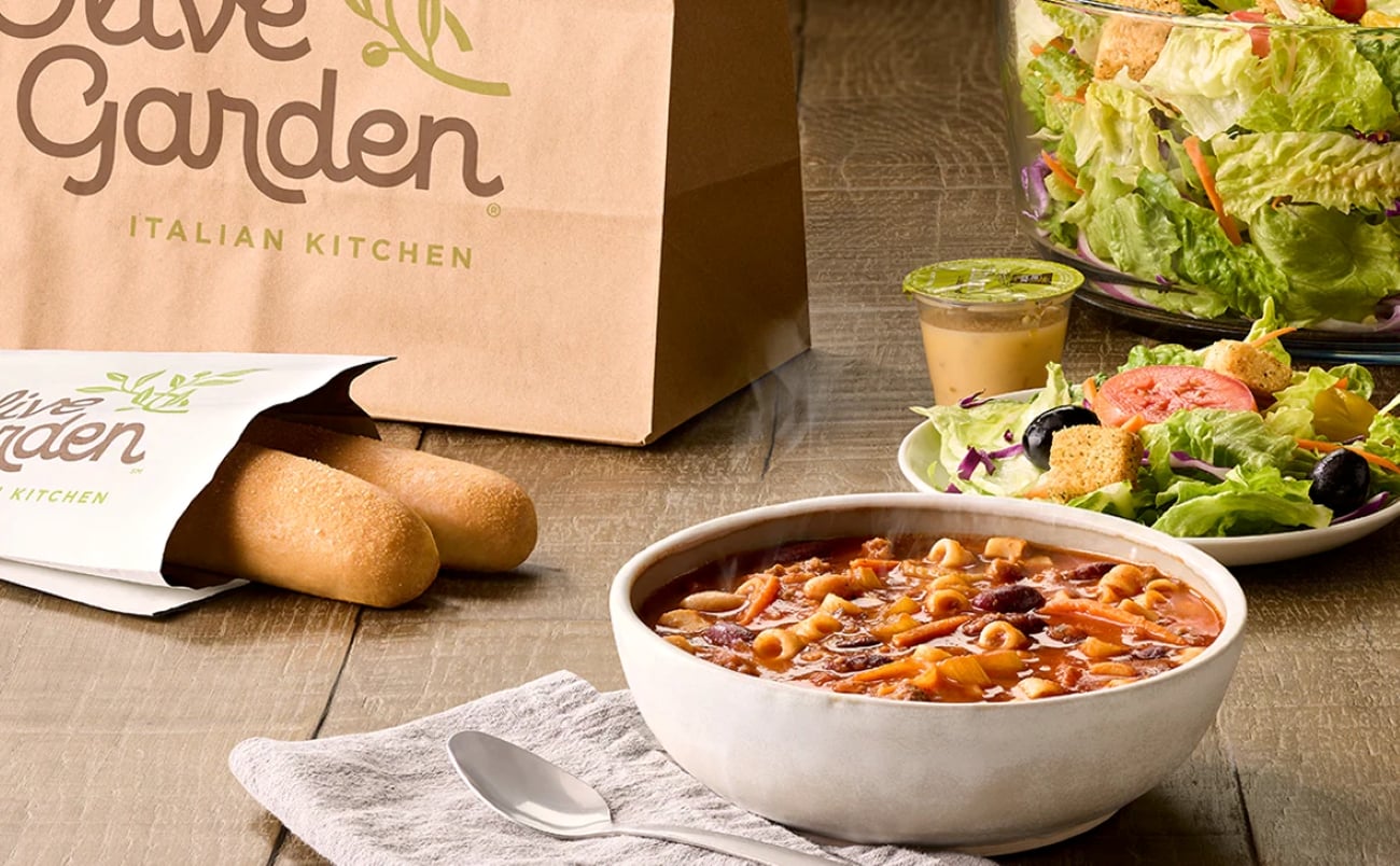 Olive Garden takeout meal featuring a bowl of pasta e fagioli soup, breadsticks, and garden salad.