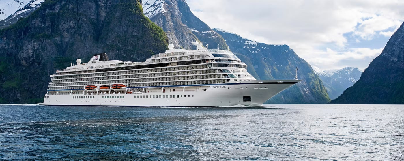 A white Viking Star cruise ship sailing through a deep blue fjord surrounded by towering, snow-capped mountains, where passengers enjoy cruise ship buffets.
