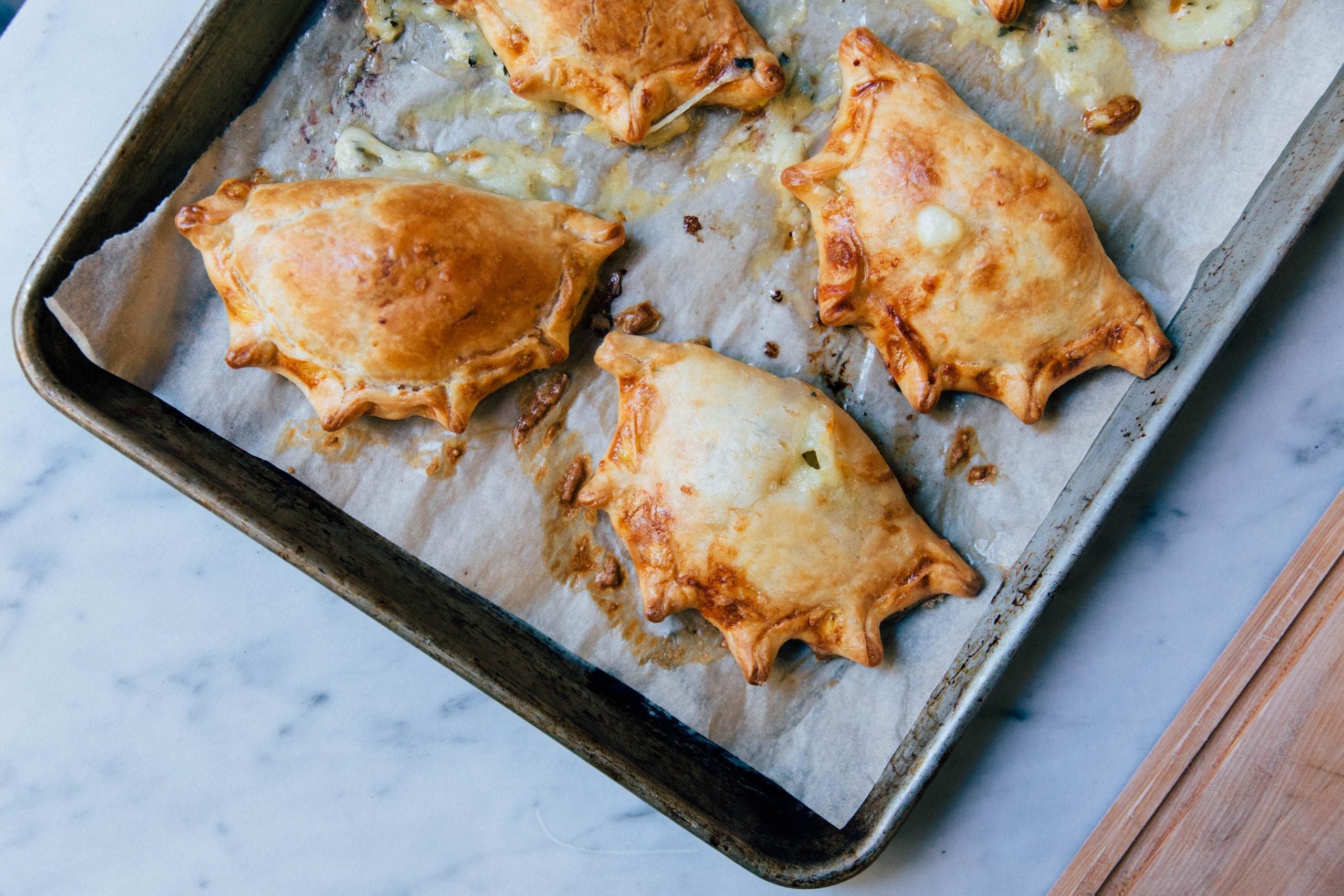 Four golden-brown baked pastries with crimped edges on a parchment-lined baking sheet.