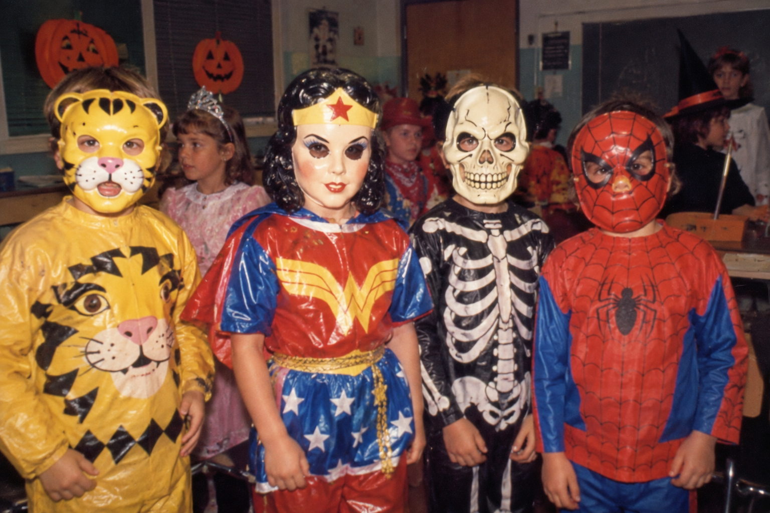 Four children in Halloween costumes wearing plastic masks of a tiger, Wonder Woman, a skeleton, and Spider-Man. Halloween at School in the '80s.