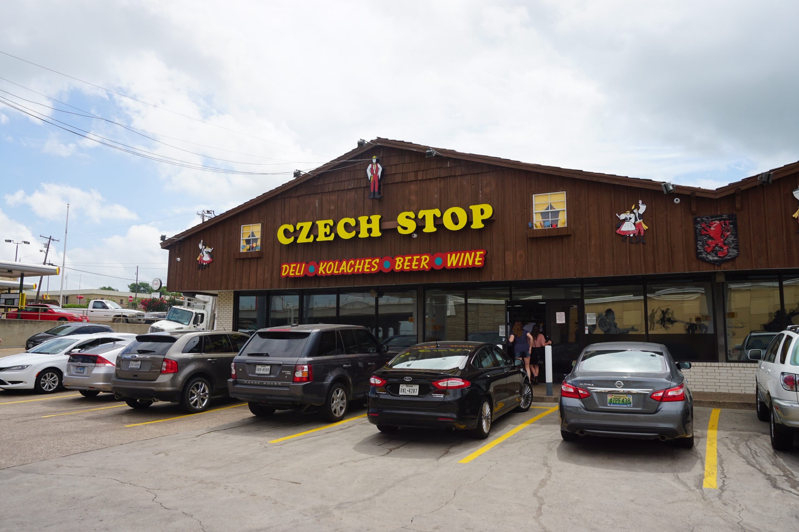 The storefront of the Czech Stop bakery, with cars parked in the foreground and people entering the building.