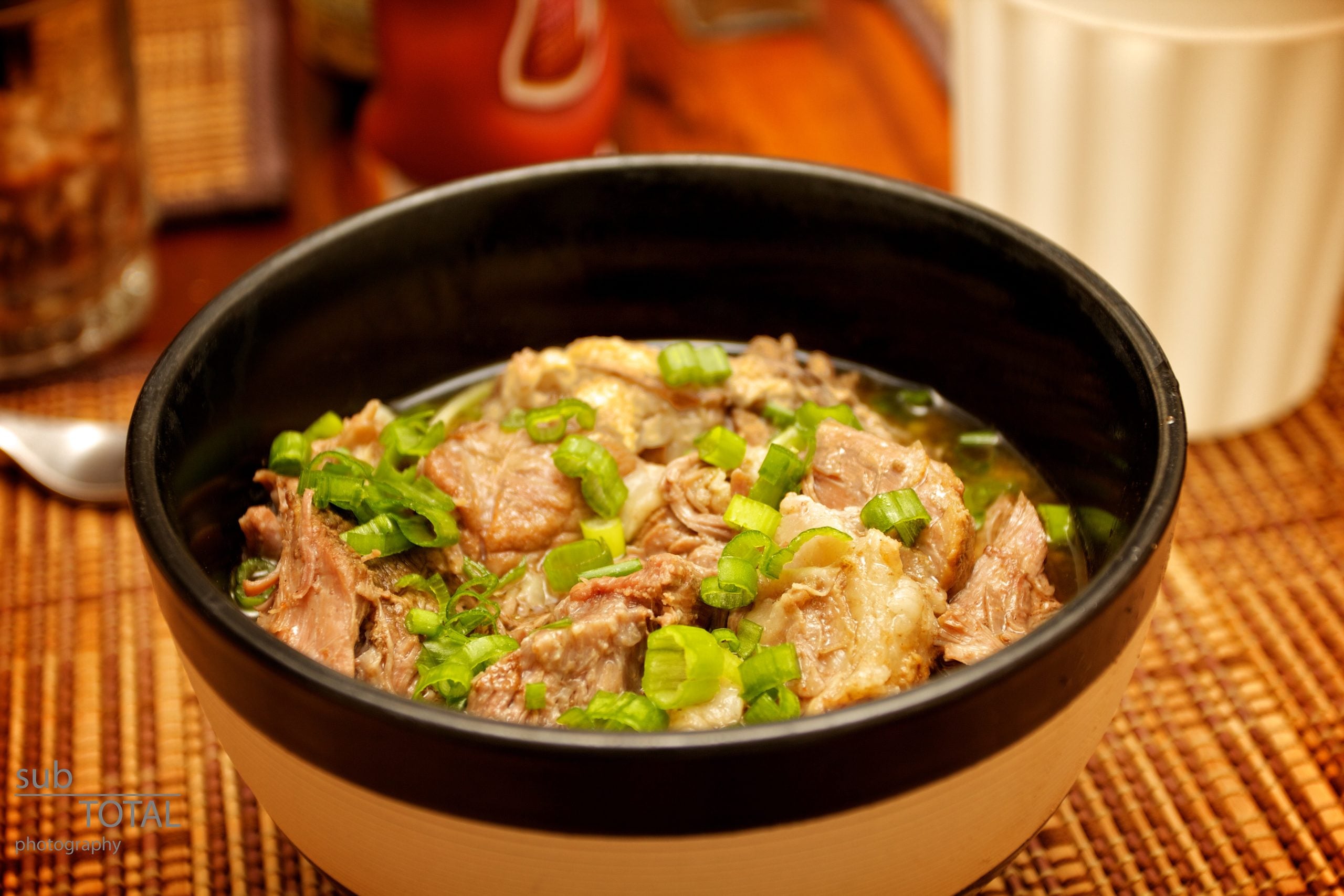 A bowl of braised meat in broth topped with sliced green onions.