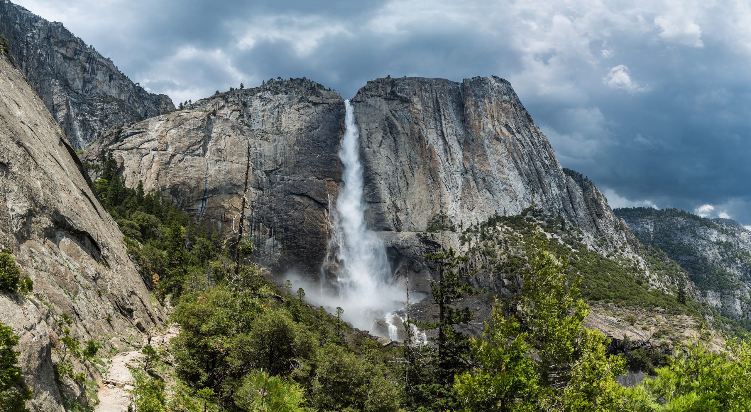 Upper Yosemite Fall cascades down a massive granite cliff face under a dramatic, cloudy sky typical of trips where bad weather occurs.