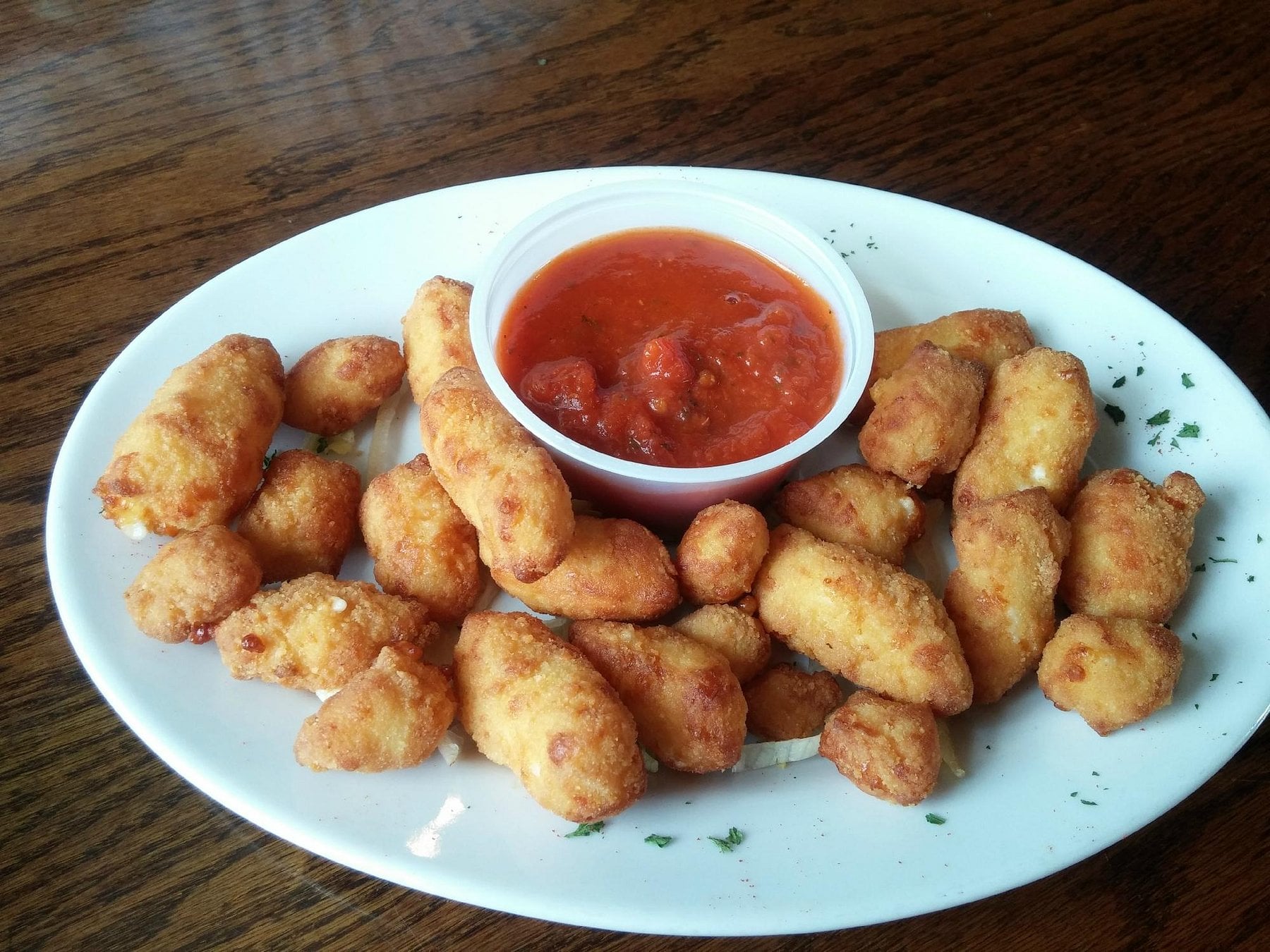 A plate of breaded mozzarella bites served with a side of marinara sauce.