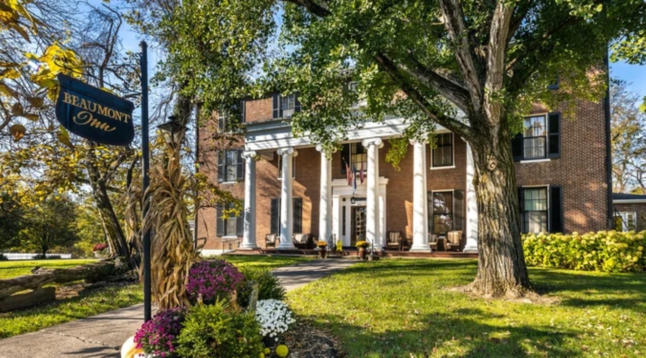 Beaumont Inn, a two-story brick building with white columns and a porch, seen from a lawn with a sign and large trees.