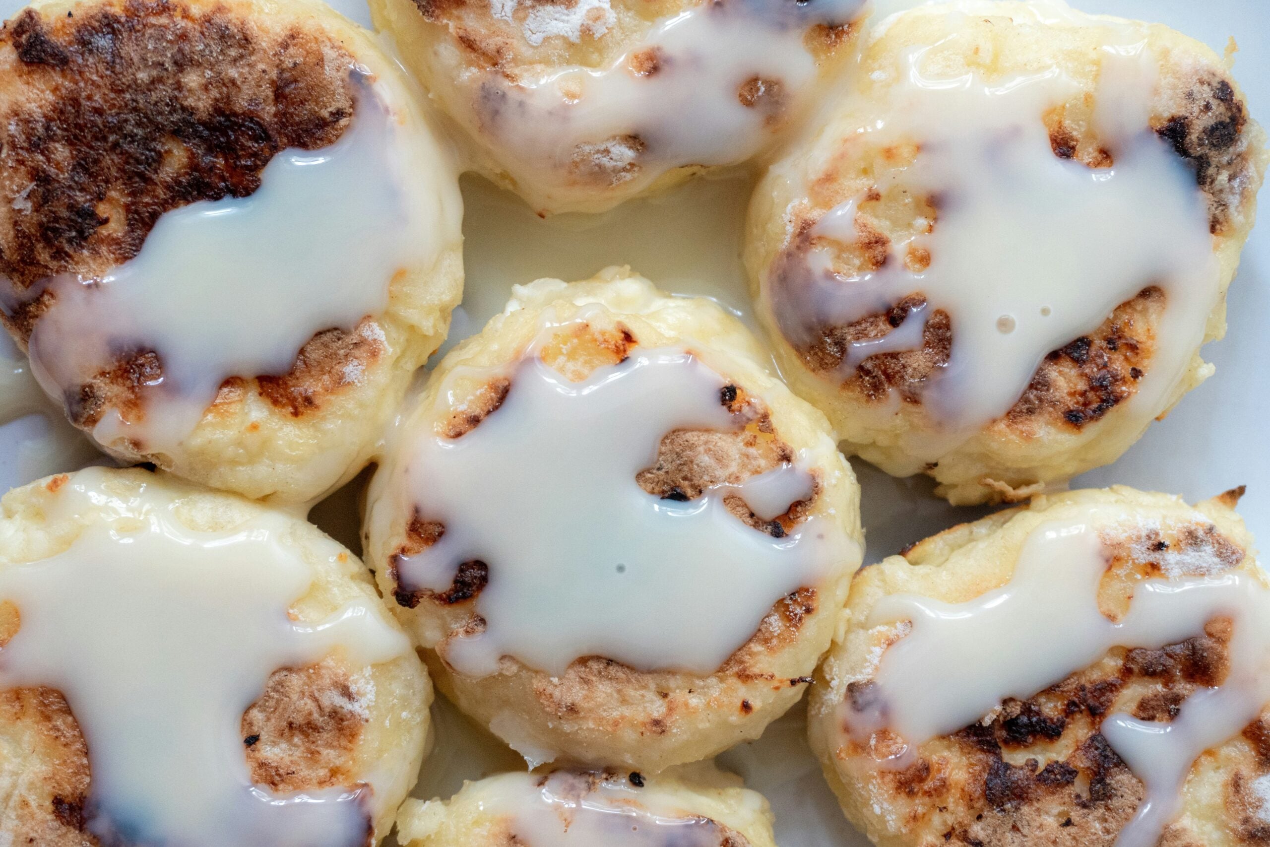 Several round, pan-fried cheese pancakes topped with a drizzle of white sauce.