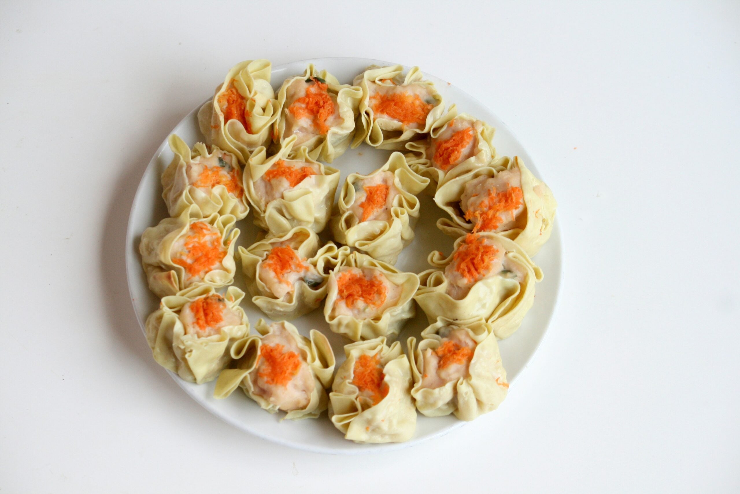 A white plate filled with steamed dumplings topped with shredded orange carrots.