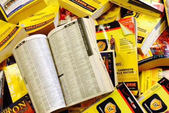A pile of yellow phone books, with one open to the business listings page.