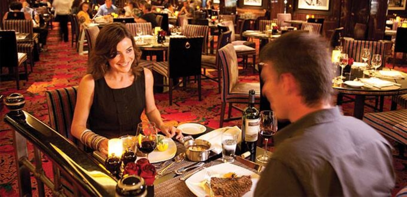 A woman smiling at her dinner companion at a table in a crowded, warmly lit restaurant.