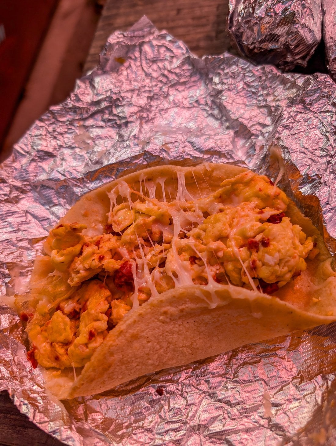 A breakfast taco filled with scrambled eggs and melted cheese in a flour tortilla, sitting on a piece of aluminum foil.