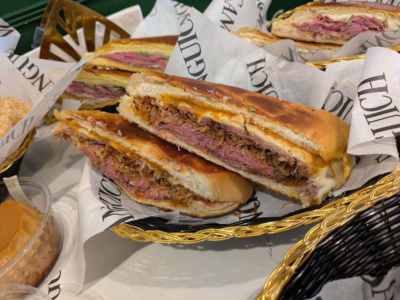 Two halves of a pressed sandwich filled with sliced meat, crispy onions, and melted cheese in a lined basket.