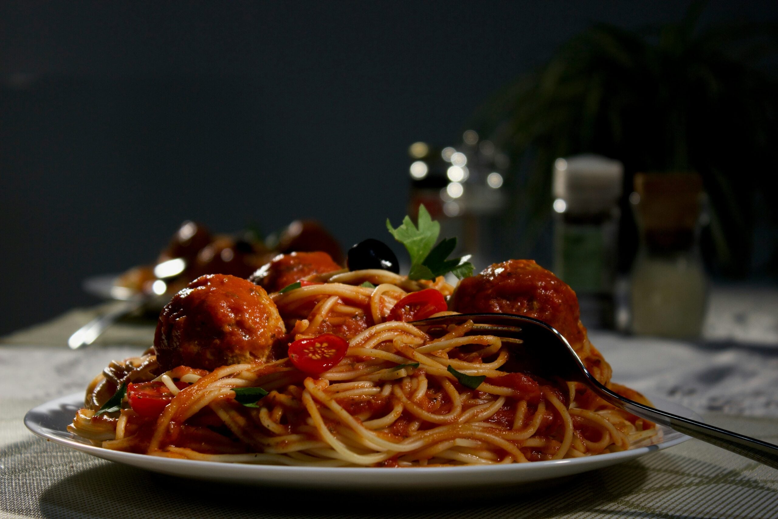 A plate of spaghetti with meatballs, tomato sauce, cherry tomatoes, and a black olive, with a fork resting on the side.