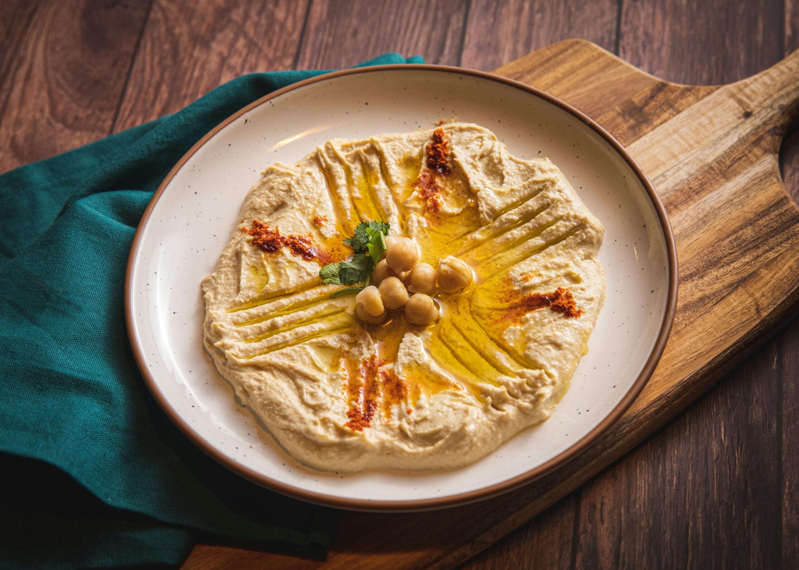 Hummus topped with olive oil, whole chickpeas, paprika, and herbs on a plate.