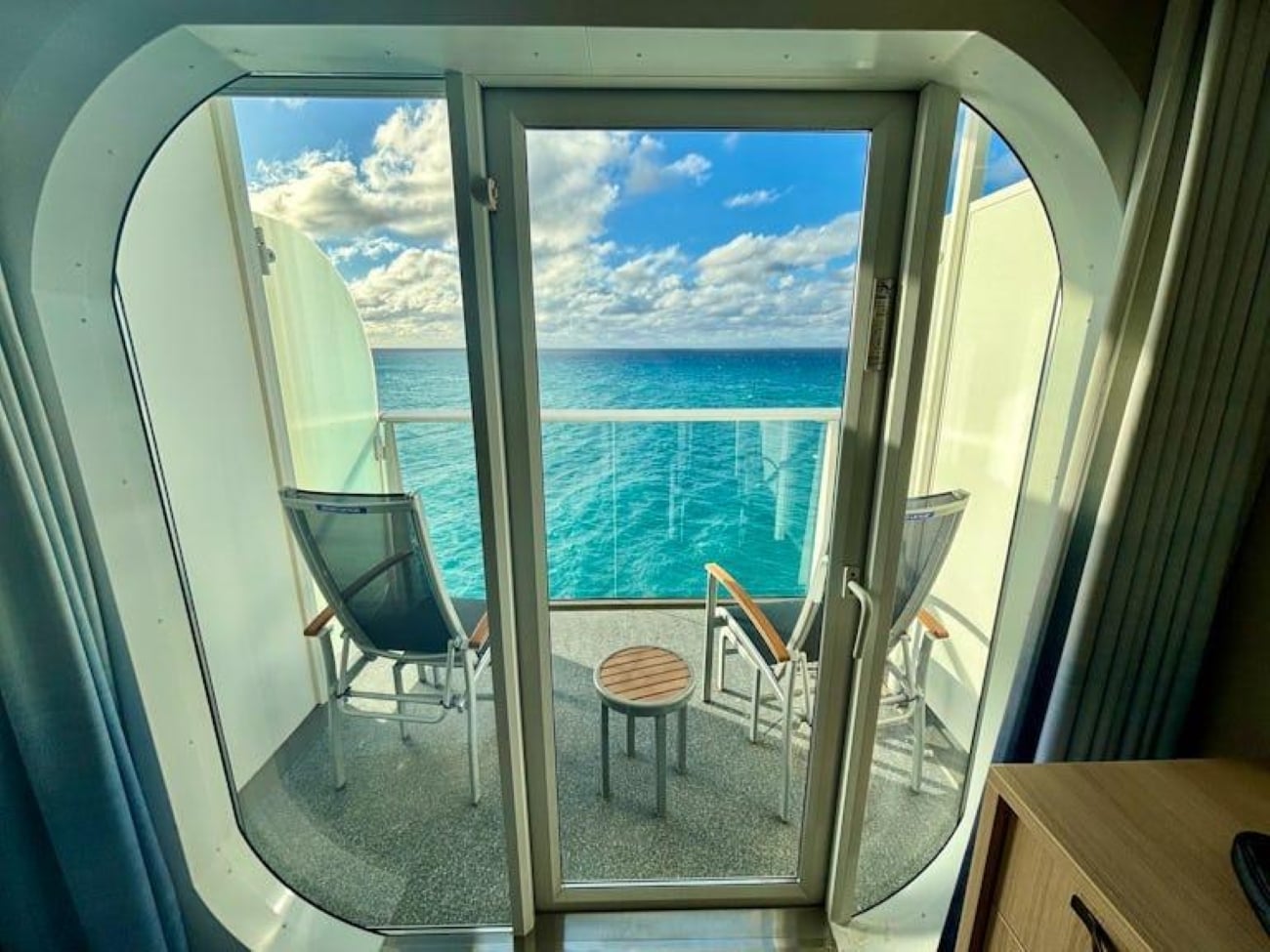 A cruise ship balcony with two chairs and a small table overlooking the ocean.
