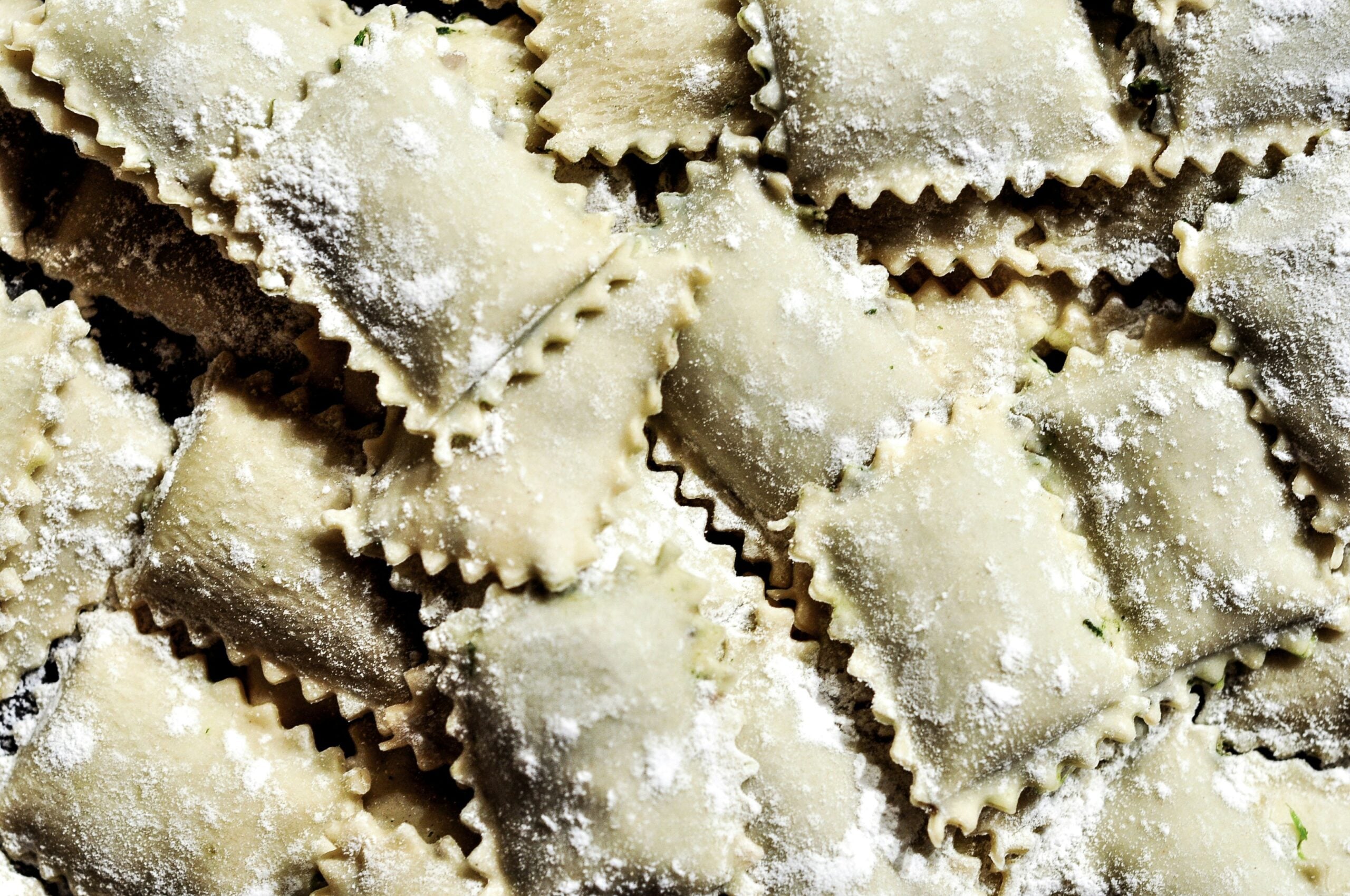 A pile of rectangular, ruffled-edge ravioli dusted with flour.