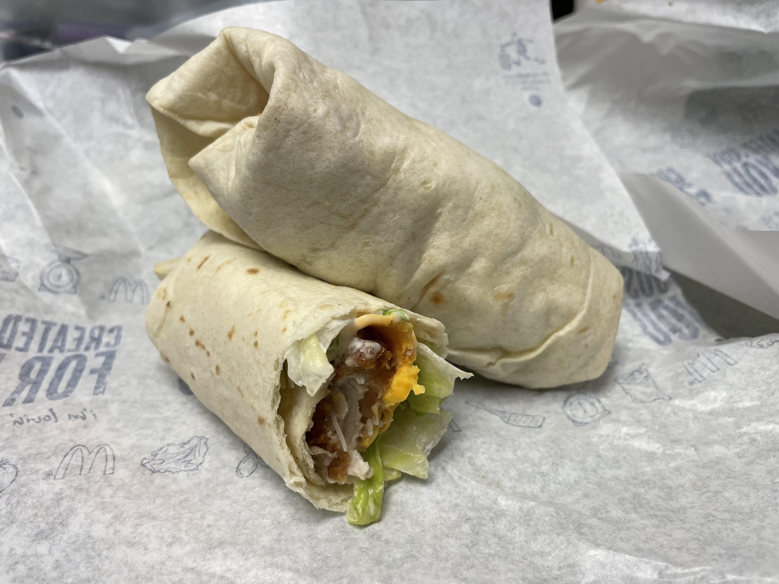 Two flour tortilla wraps on patterned parchment paper, one sliced to show a filling of chicken, lettuce, and cheese.