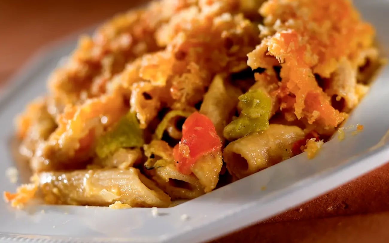 Baked pasta casserole with vegetables topped with a golden-brown breadcrumb crust on a white plate.