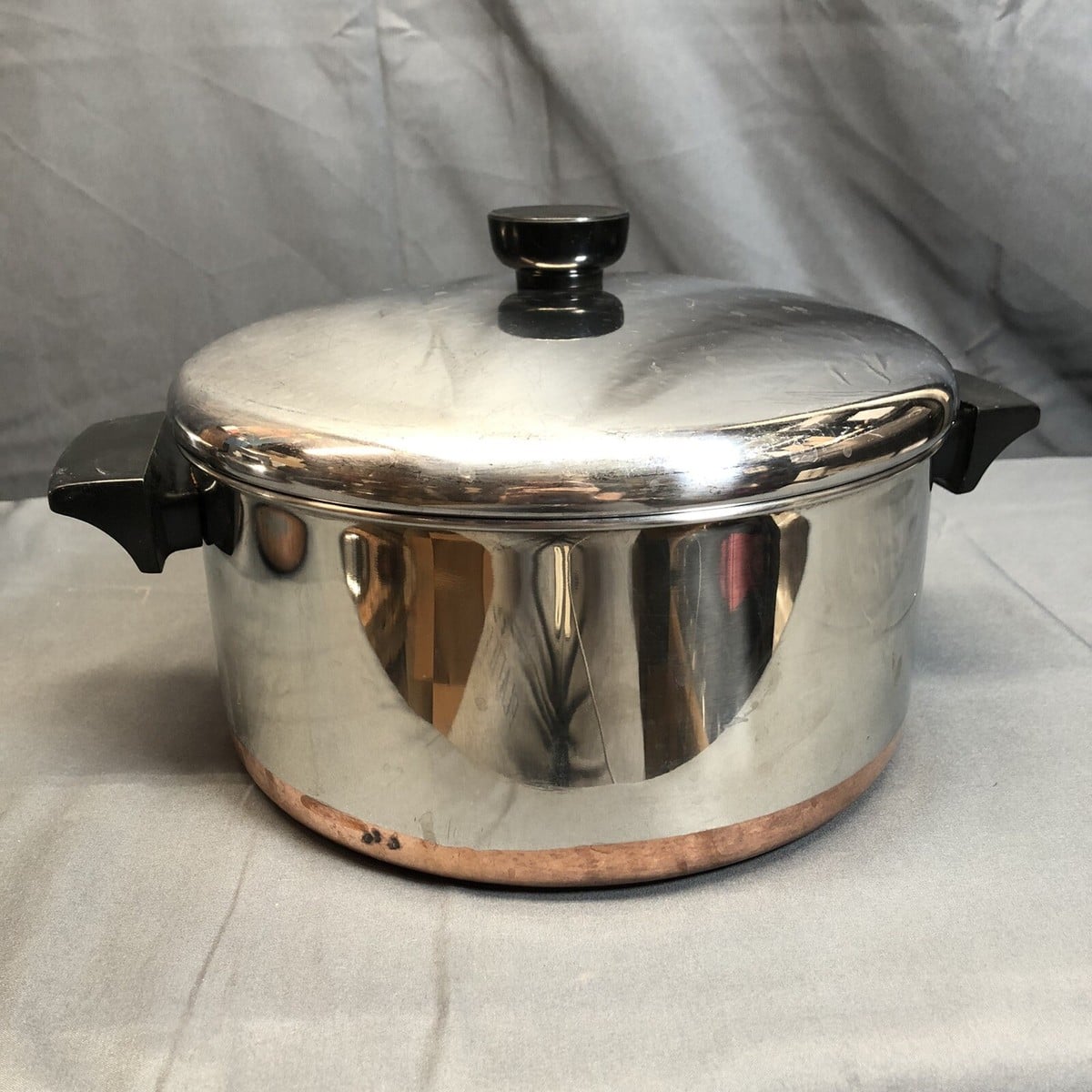 A stainless steel pot with a copper base, black handles, and a matching lid.