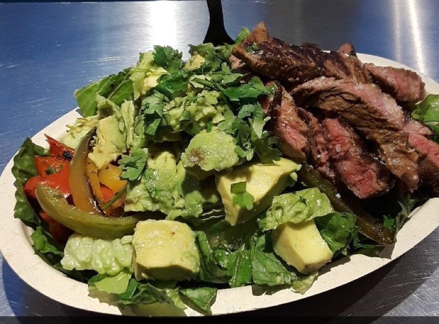 A salad bowl containing sliced steak, avocado, greens, and sautéed peppers.