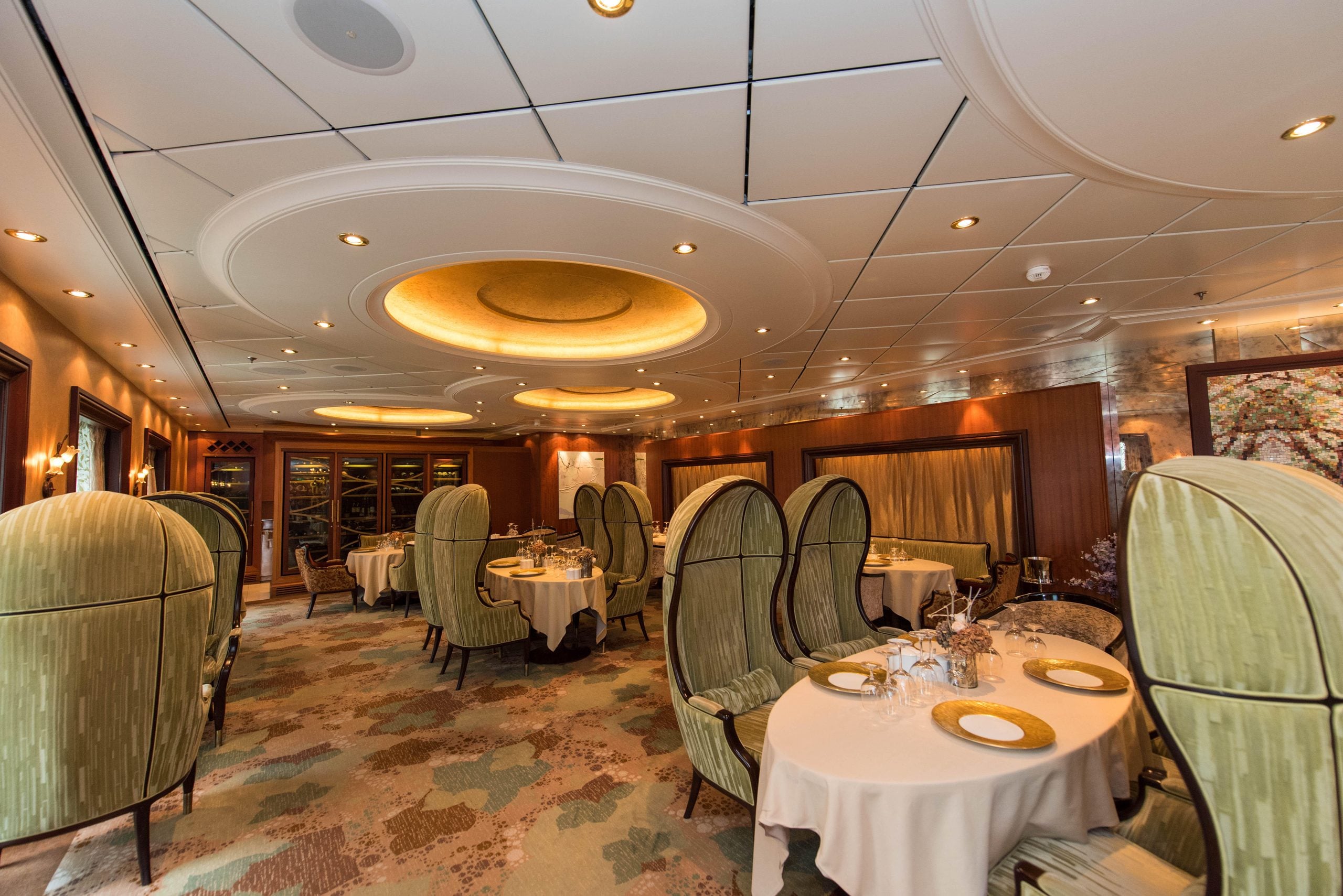 A fine dining restaurant interior featuring tables with light-colored tablecloths and high-backed, cocoon-style velvet chairs.