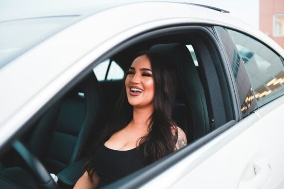 A smiling woman sitting in the driver’s seat of a white car.