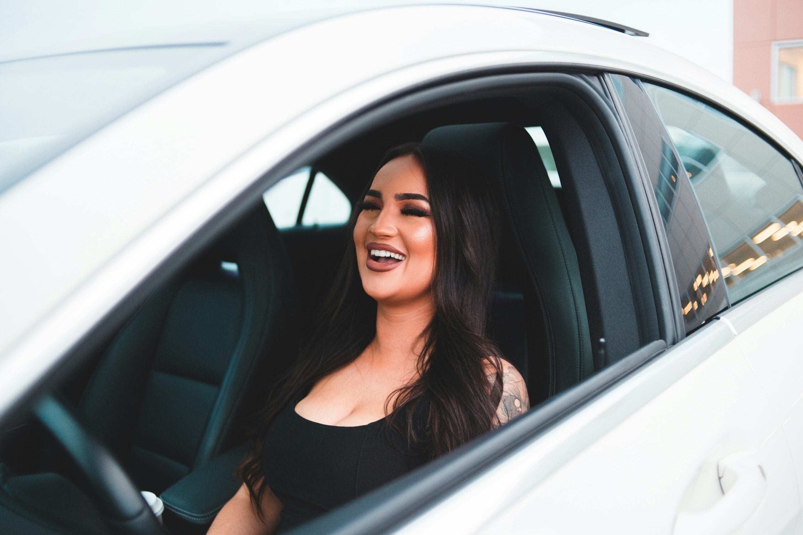 A smiling woman sitting in the driver’s seat of a white car.