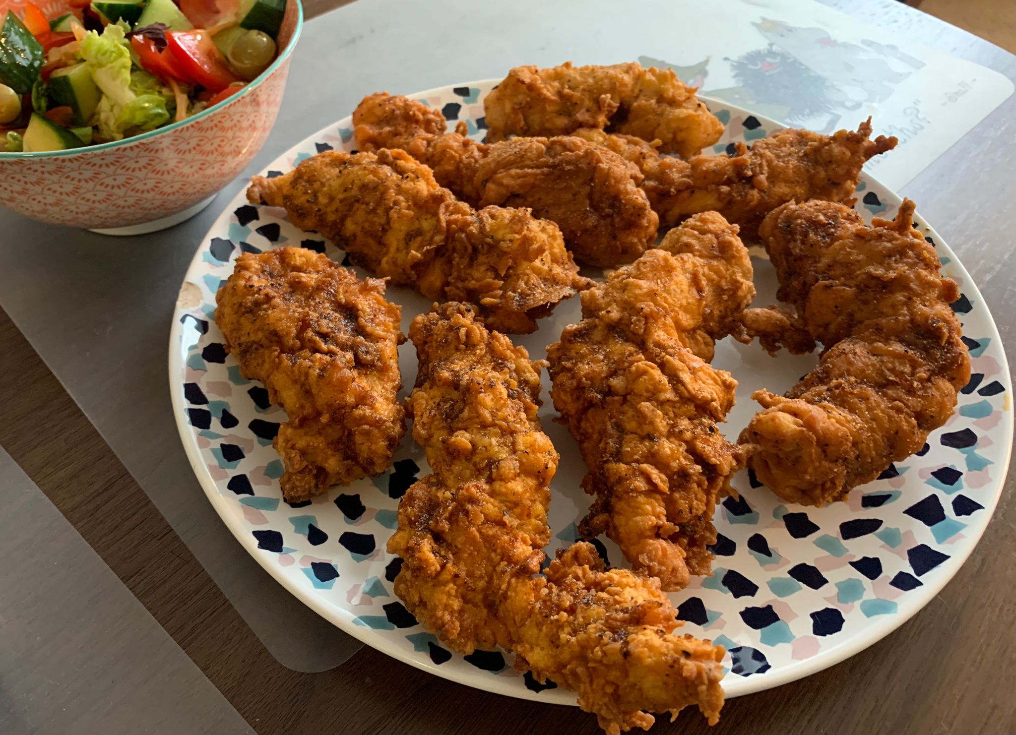 A plate of fried chicken tenders next to a bowl of salad.