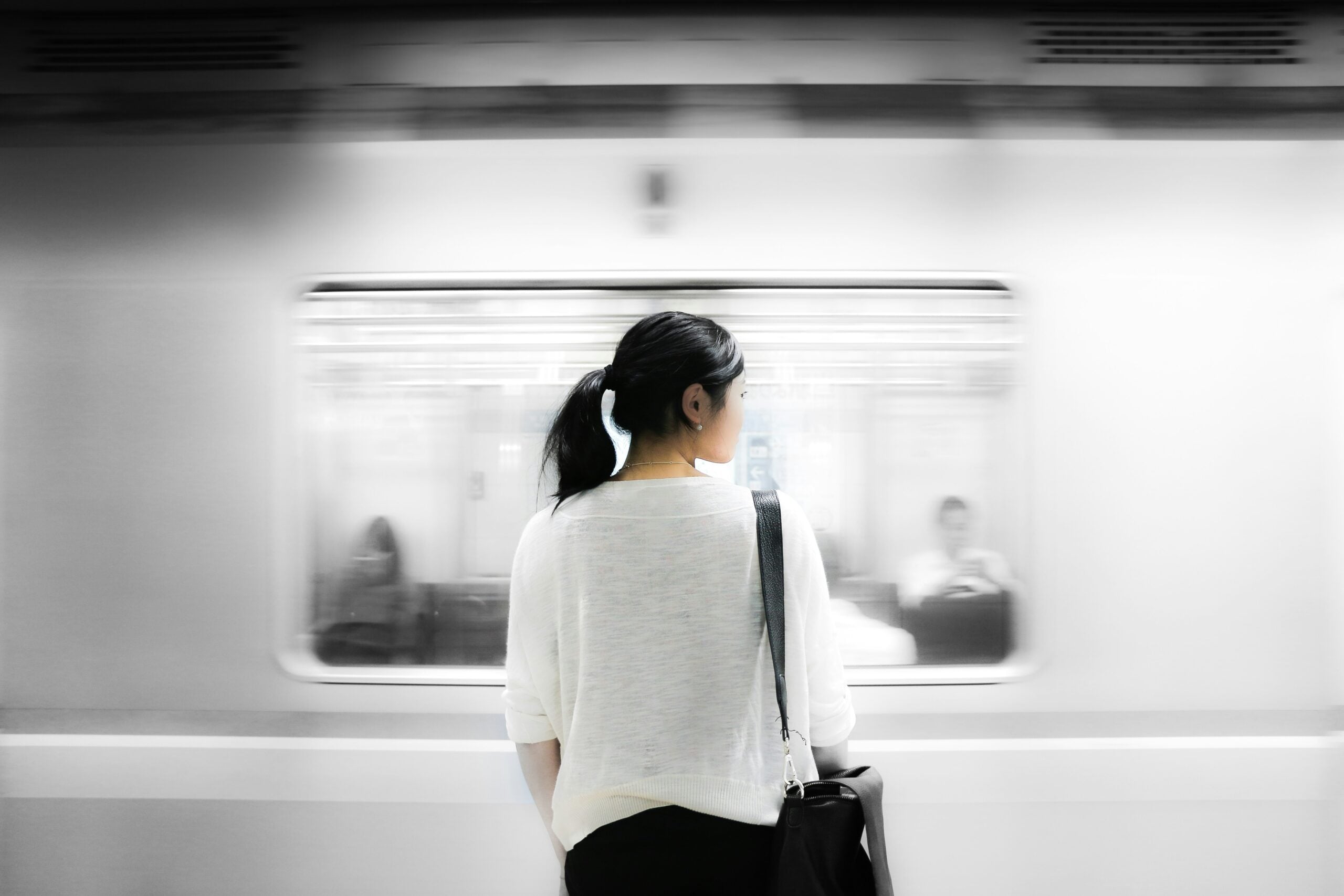 A woman seen from behind stands on a subway platform watching a train pass by.