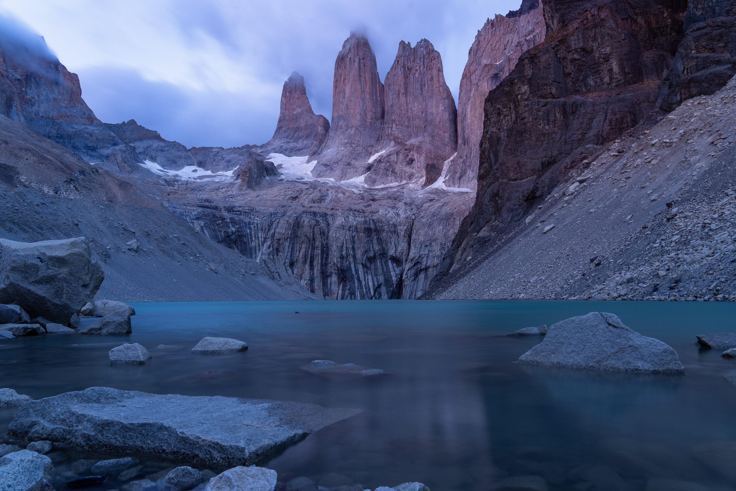 The three jagged granite towers of Torres del Paine rising above a calm, turquoise glacial lake.
