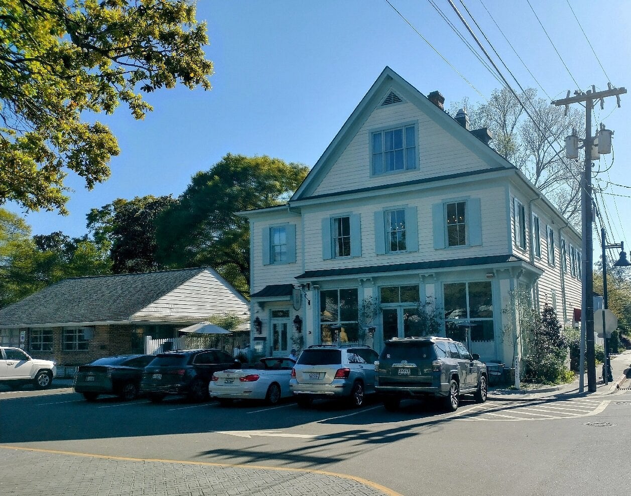 A two-story, cream-colored building with light blue shutters and trim, featuring a restaurant on the ground floor with cars parked in front.