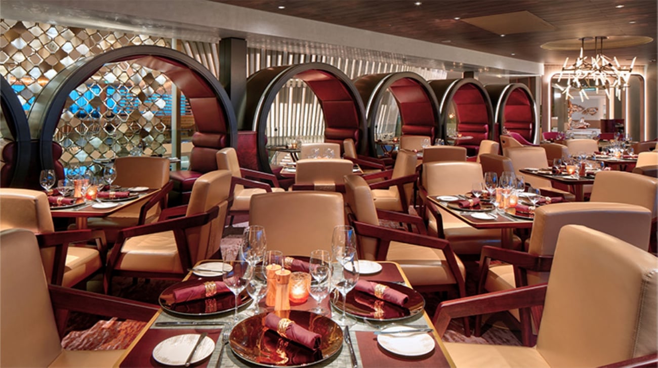A high-end restaurant interior featuring leather chairs, wooden tables set for dinner, and distinctive circular, semi-enclosed booth seating.