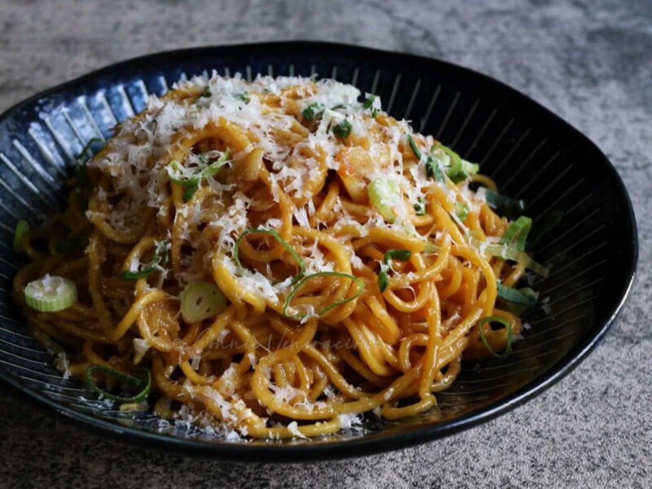A bowl of saucy noodles topped with grated cheese and sliced green onions.