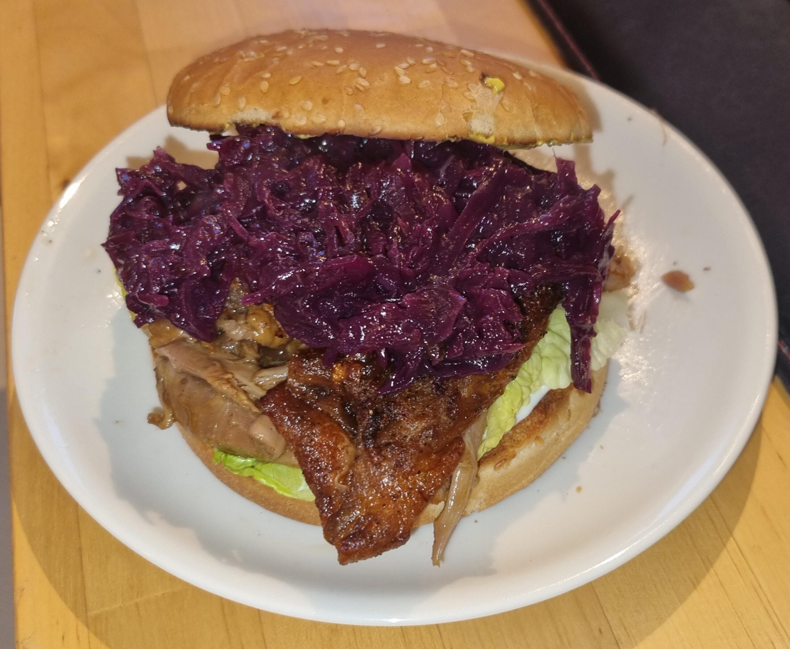 A pork sandwich on a sesame seed bun, topped with a large portion of braised red cabbage.