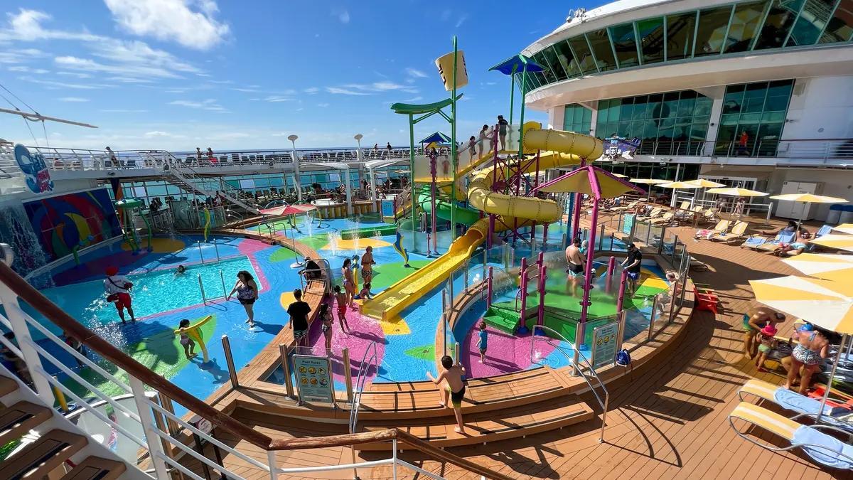People swimming and playing on a cruise ship deck with yellow waterslides and a splash pad.