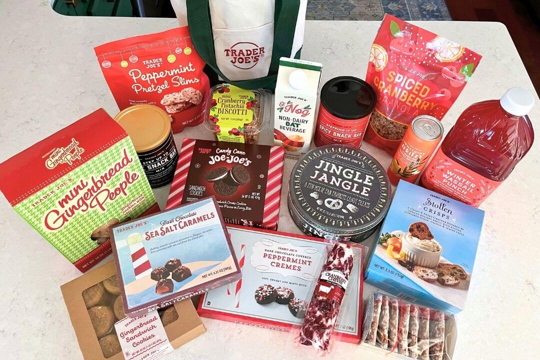 A collection of Trader Joe’s holiday-themed snacks, including peppermint pretzels, gingerbread cookies, Jingle Jangle mix, chocolate caramels, peppermint cremes, and a bottle of Winter Wassail Punch. Trader Joe's holiday shopping hacks.