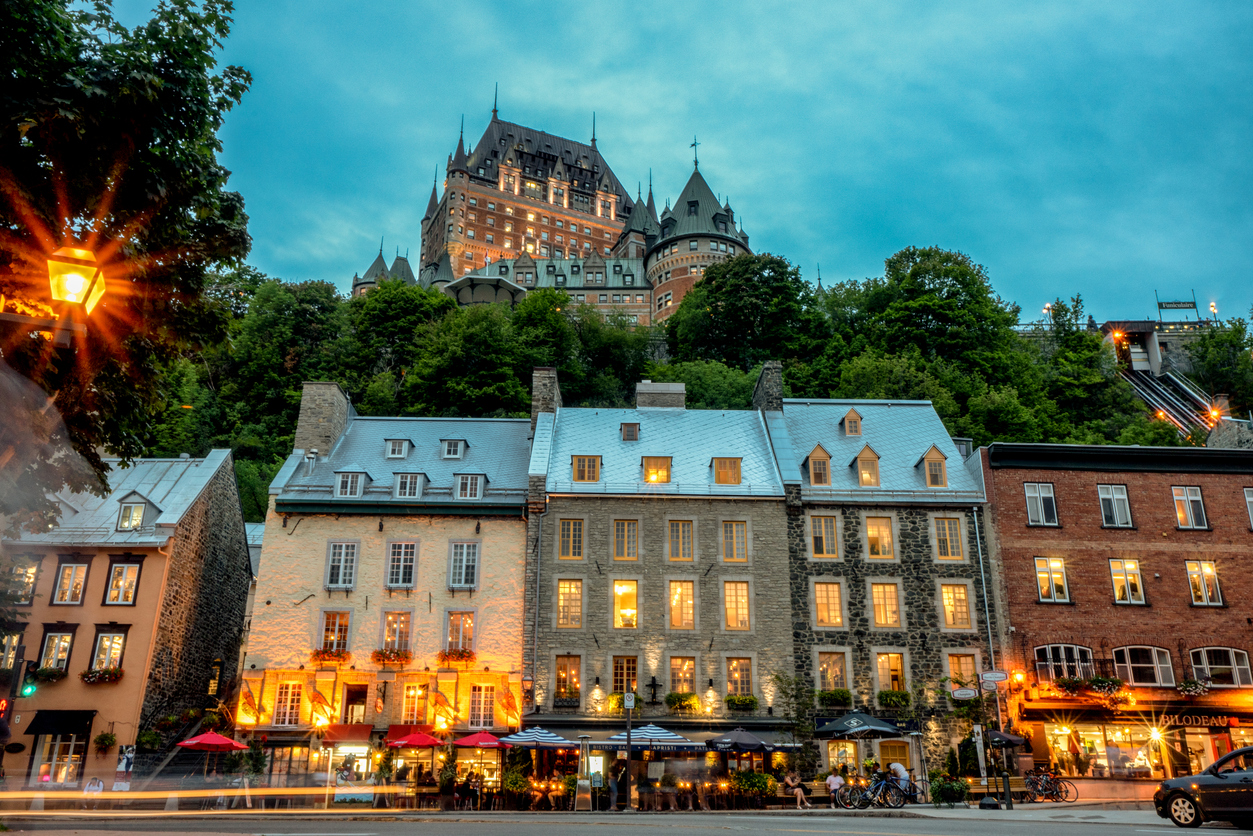 The Fairmont Le Château Frontenac sits atop a cliff overlooking stone buildings and illuminated storefronts in historic Old Quebec, offering a getaway for trips that feel luxurious.