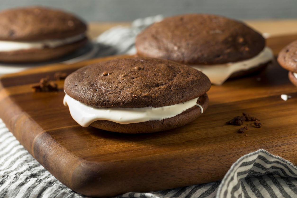 Three chocolate whoopie pies, a classic among regional desserts, served with white cream filling on a wooden cutting board.
