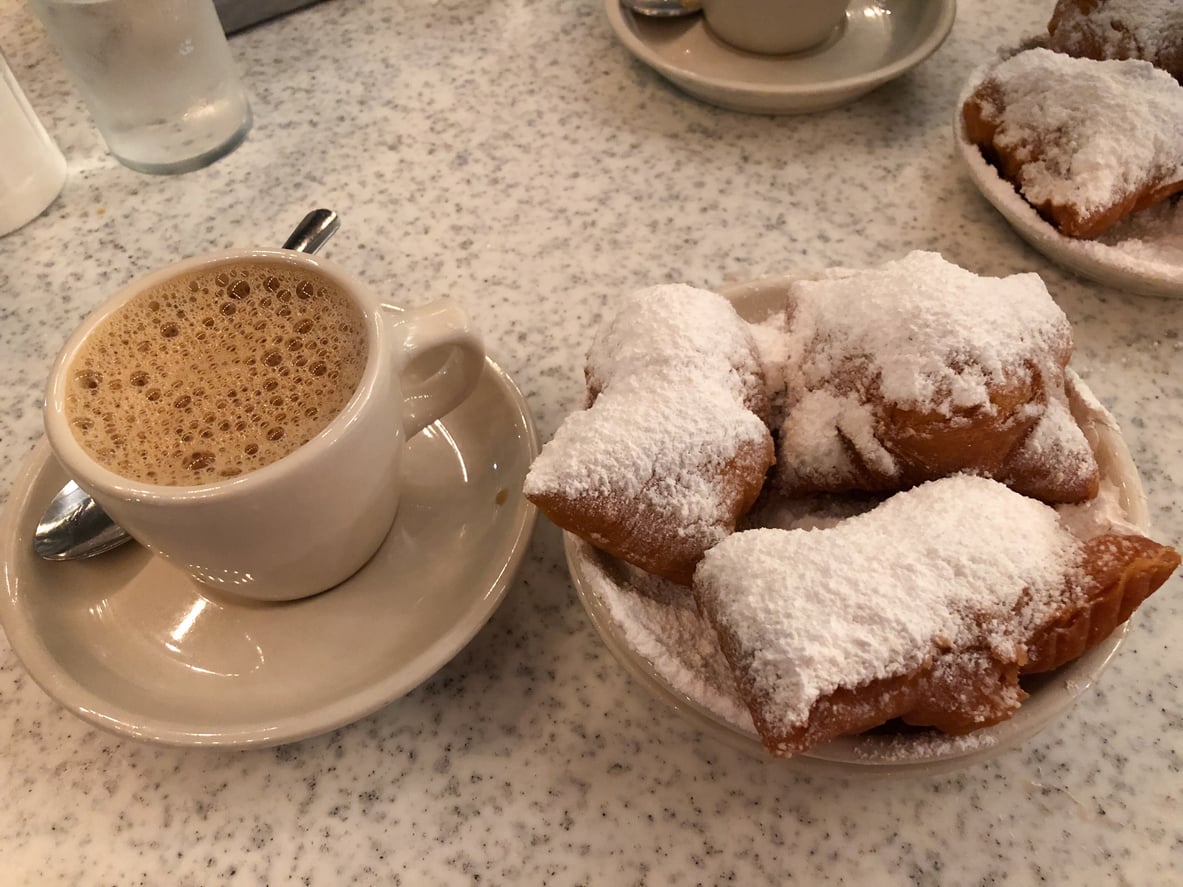 A cup of café au lait next to a plate of beignets covered in powdered sugar.
