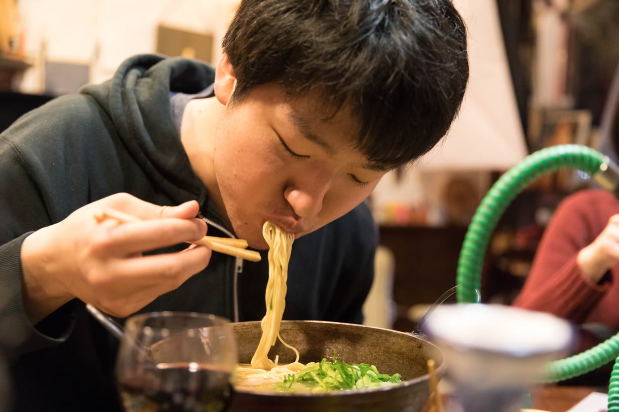 A man eats noodles from a bowl with chopsticks.