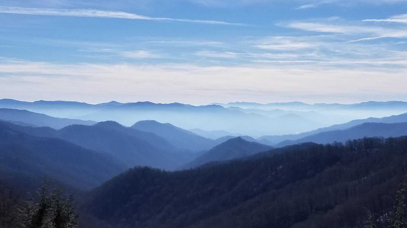 Layers of blue mountain ridges fading into a misty horizon under a pale sky.
