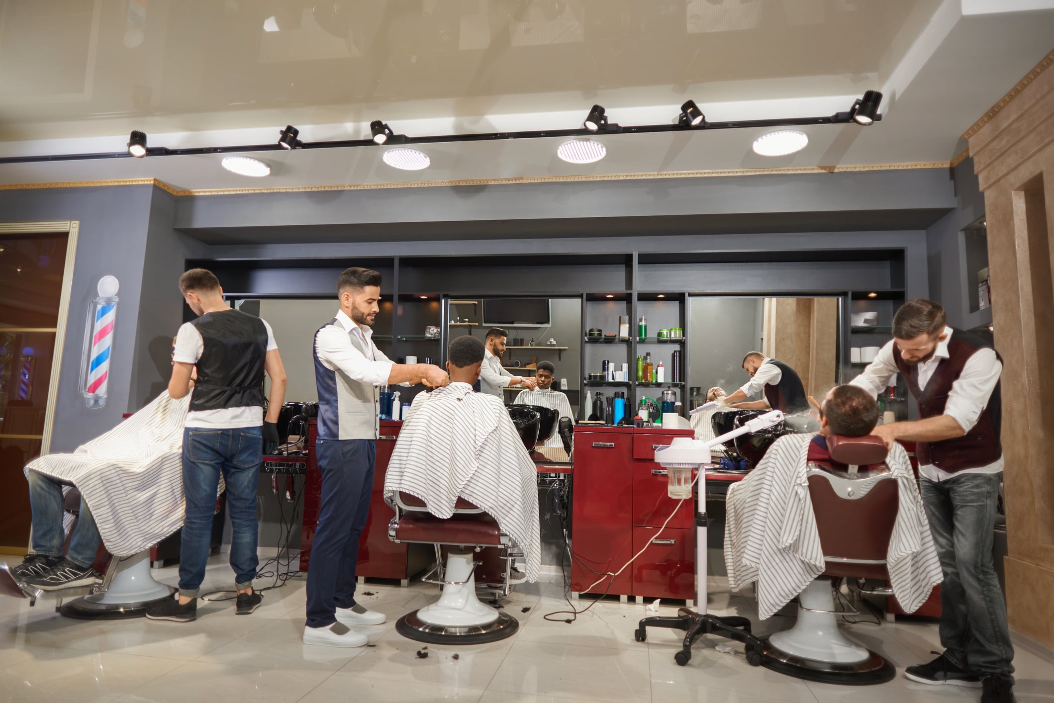 Three barbers cut the hair of clients seated in salon chairs in a modern barbershop.