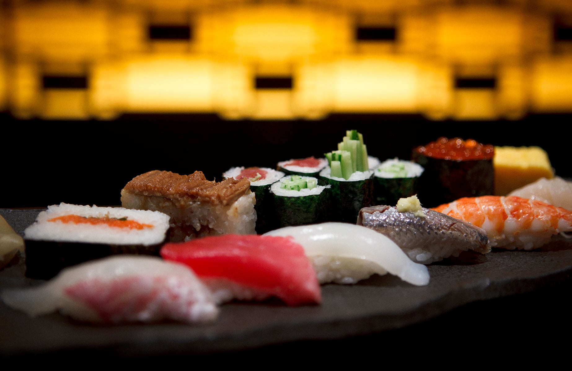 An assortment of nigiri and maki sushi rolls served on a dark stone platter.
