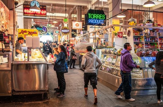 Customers and staff inside a bustling indoor food market with various stalls, signs, and produce displays.