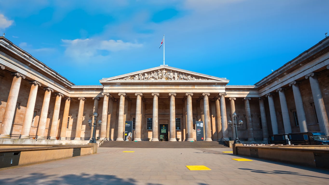 The British Museum building with its large neoclassical facade, rows of columns, and a pediment featuring sculptures, viewed from the front plaza.