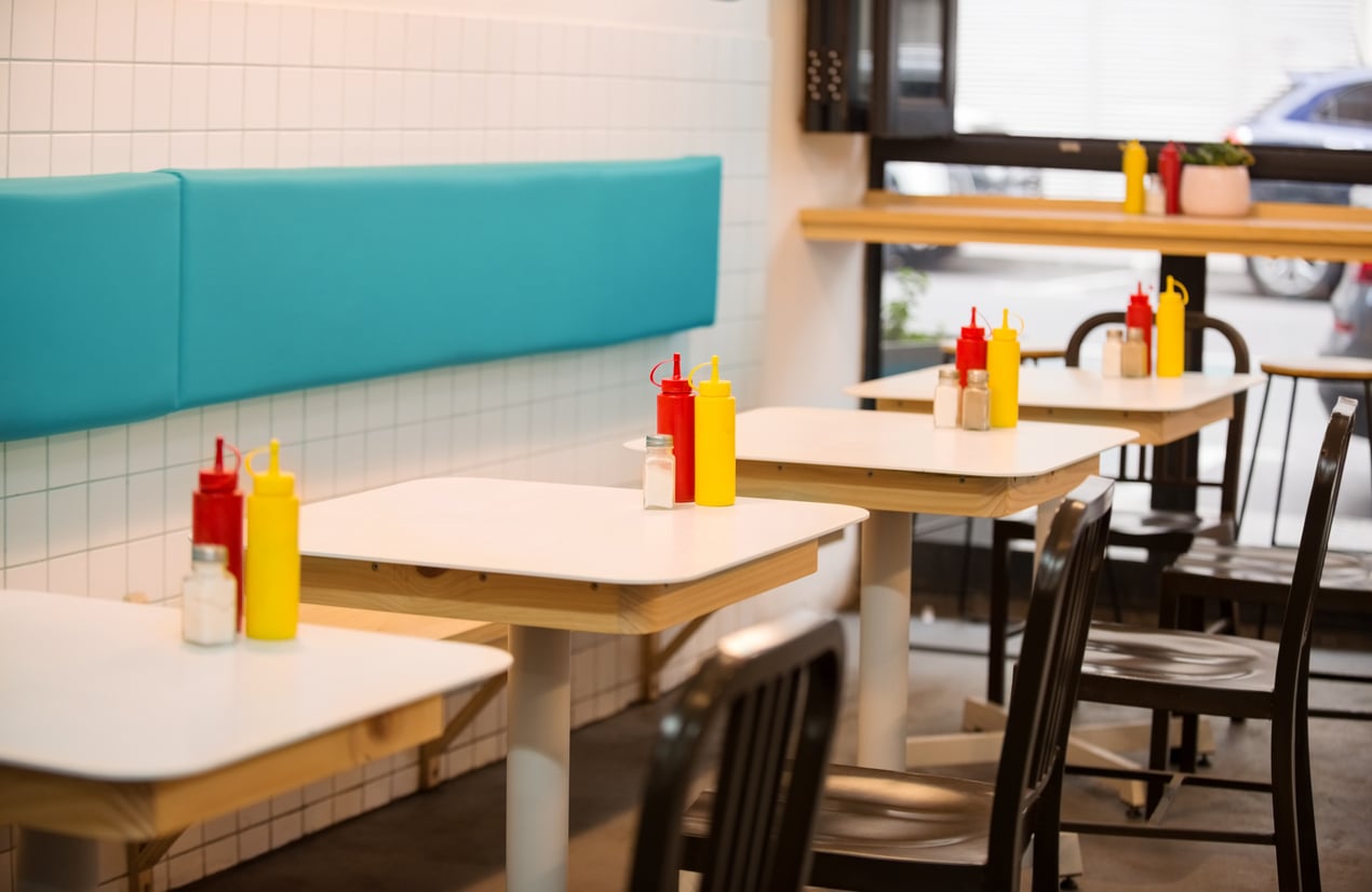 Rows of white tables in a diner, each with a yellow mustard bottle, a red ketchup bottle, and a salt shaker.