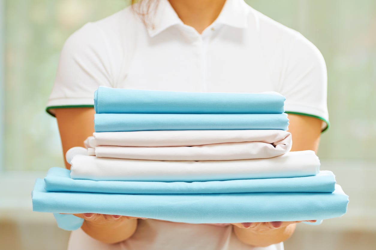 A person holding a stack of neatly folded light blue and white bed sheets, similar to those managed under cruise ship charges.