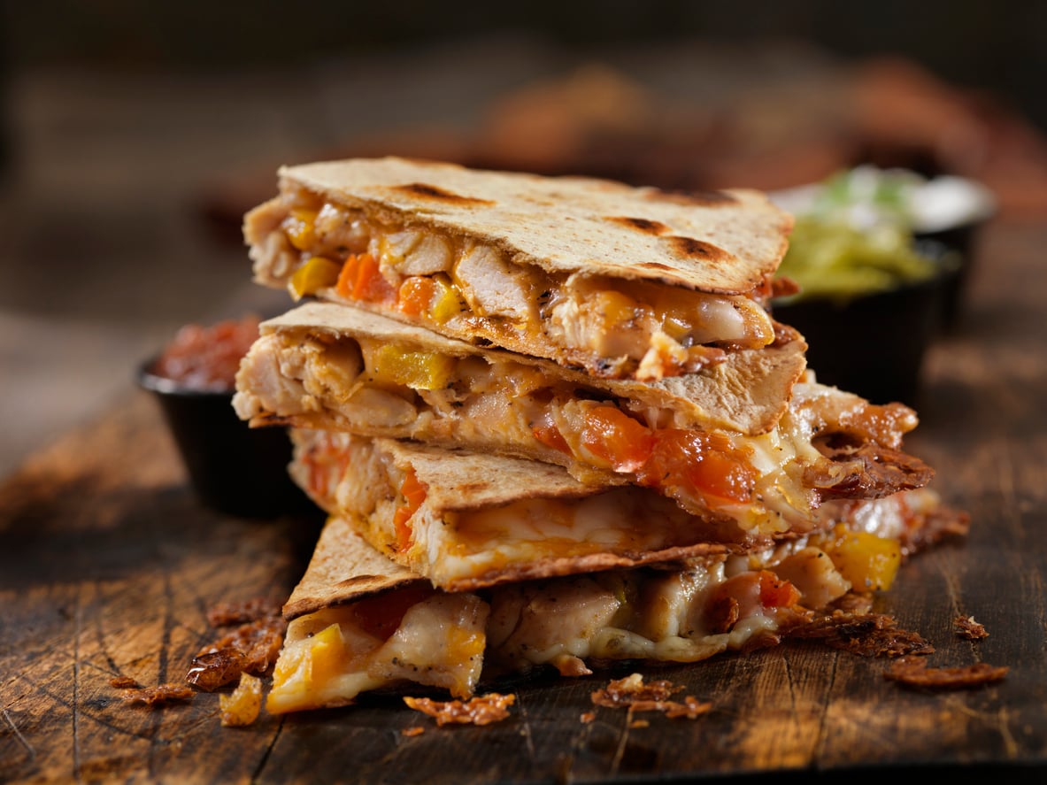 A stack of four chicken and cheese quesadilla wedges on a wooden board.