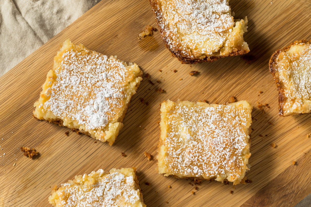 Four square lemon bars dusted with powdered sugar on a wooden cutting board.