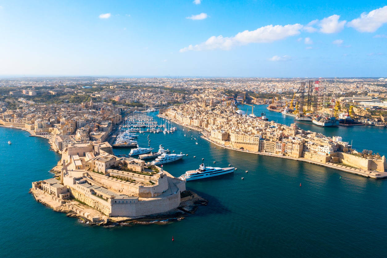 Aerial view of the Grand Harbour in Valletta, Malta, featuring Fort St. Angelo in the foreground and a harbor filled with yachts and ships surrounded by historic stone buildings.