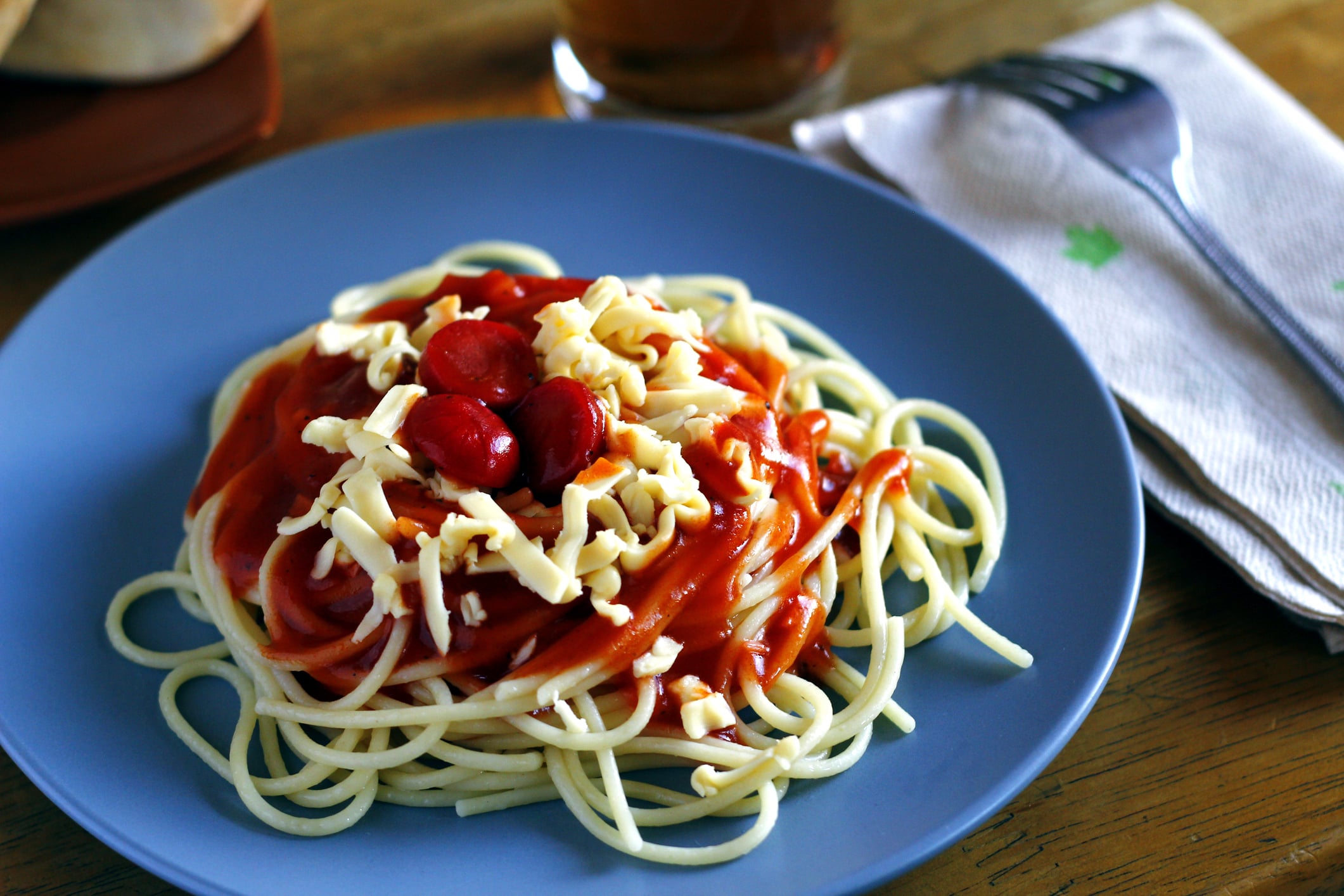 Spaghetti topped with tomato sauce, sliced sausage, and shredded cheese on a blue plate.